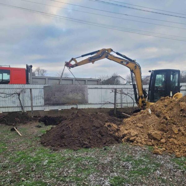 Міні-екскаватор CAT 303.SE встановлює бетонне кільце для септика